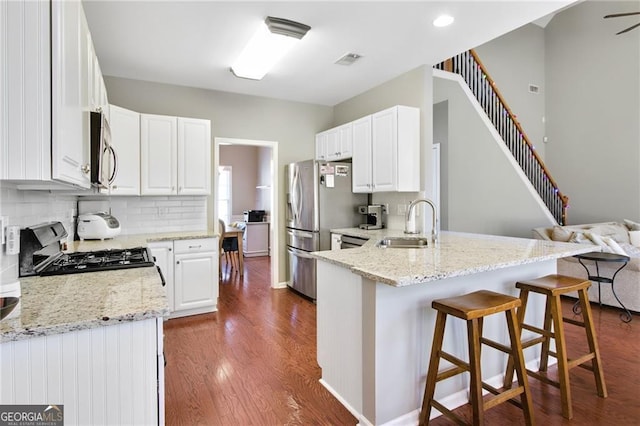 kitchen featuring kitchen peninsula, appliances with stainless steel finishes, light stone counters, white cabinets, and dark hardwood / wood-style floors