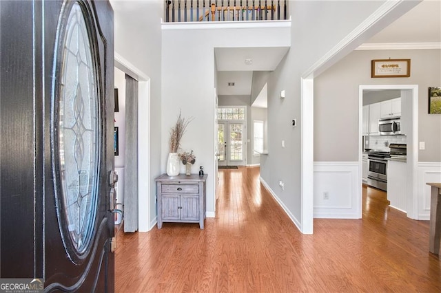 entryway with french doors, light hardwood / wood-style floors, a high ceiling, and ornamental molding