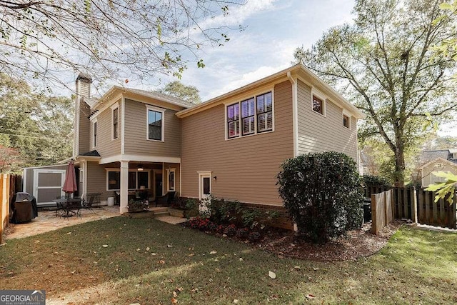 rear view of house featuring a yard, a storage unit, and a patio area