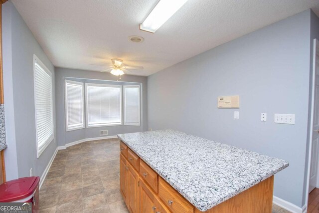 611 Bernhard Rd, Fayetteville, GA 30215 - kitchen with ceiling fan, light stone counters, a center island, and brown cabinetry