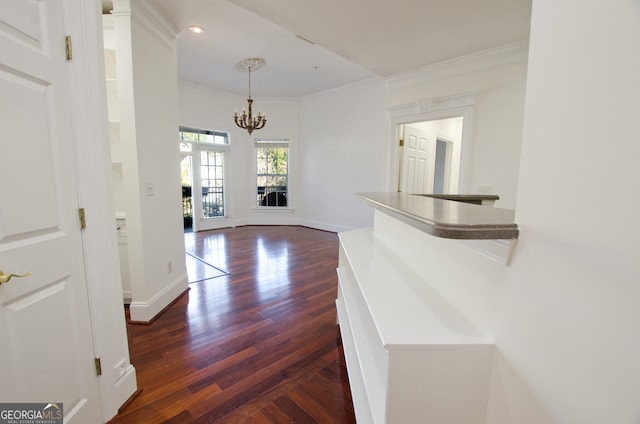 hall with crown molding, dark wood-type flooring, and an inviting chandelier