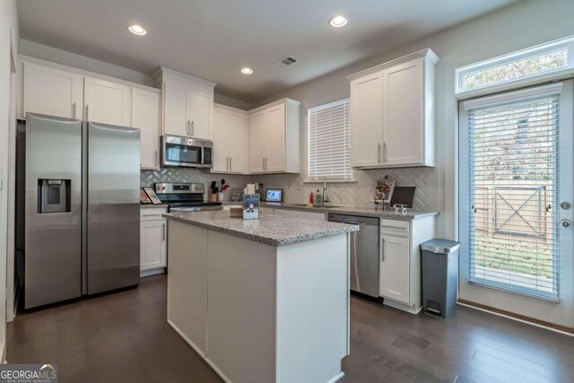 kitchen with dark hardwood / wood-style flooring, stainless steel appliances, a kitchen island, sink, and white cabinetry