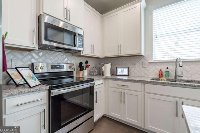 kitchen with backsplash, white cabinets, sink, light stone countertops, and stainless steel appliances