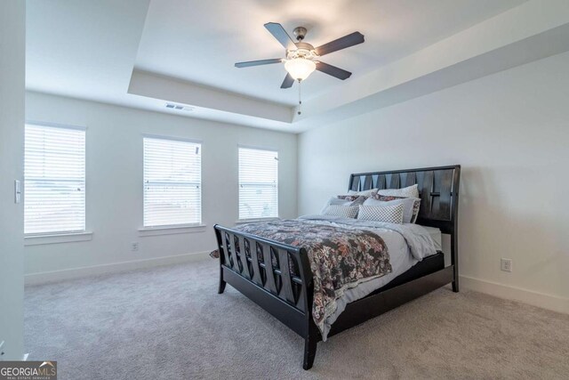 carpeted bedroom with a tray ceiling, multiple windows, and ceiling fan