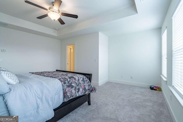 carpeted bedroom with ceiling fan and a raised ceiling