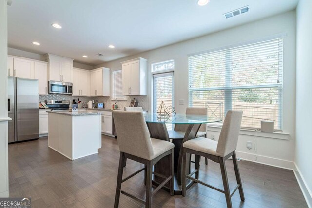 kitchen featuring appliances with stainless steel finishes, tasteful backsplash, a kitchen island, dark hardwood / wood-style floors, and white cabinetry