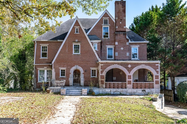 tudor-style house featuring a porch and a front yard