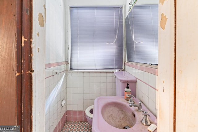 bathroom with toilet, tile patterned floors, tile walls, and sink