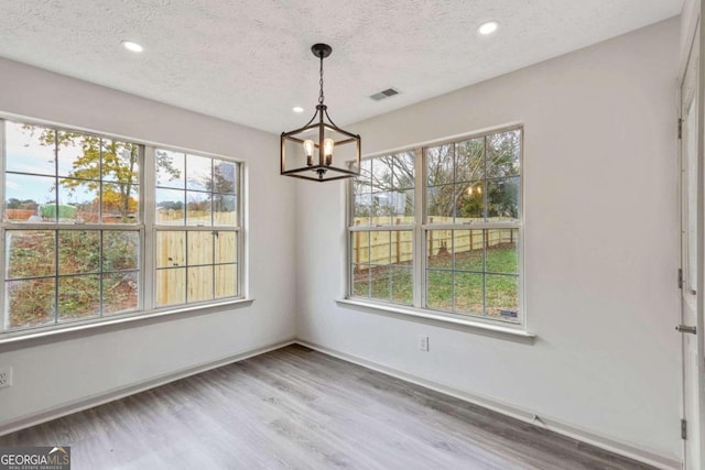 unfurnished dining area with a chandelier, wood-type flooring, and a textured ceiling