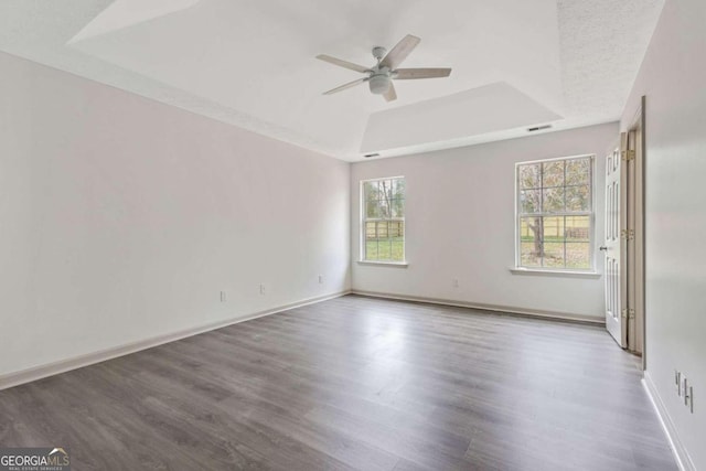 empty room featuring hardwood / wood-style flooring, ceiling fan, a wealth of natural light, and a tray ceiling