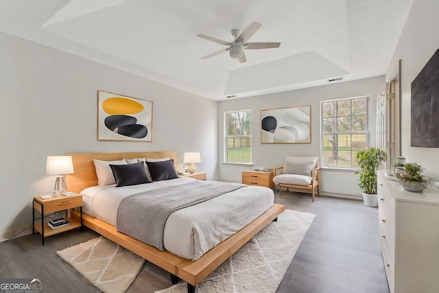 bedroom with dark hardwood / wood-style floors, a raised ceiling, and ceiling fan