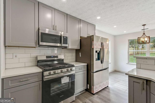 kitchen with appliances with stainless steel finishes, tasteful backsplash, gray cabinetry, dark wood-type flooring, and a chandelier