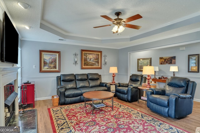 living room with ornamental molding, a textured ceiling, a tray ceiling, ceiling fan, and light hardwood / wood-style floors