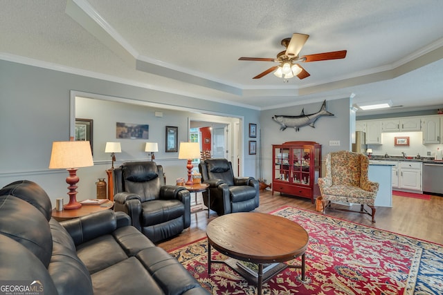 living room with ornamental molding, a tray ceiling, and light hardwood / wood-style flooring