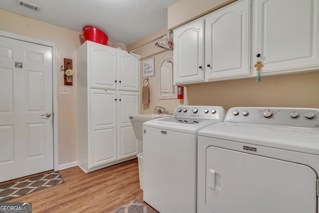 laundry room with sink, cabinets, washing machine and dryer, light hardwood / wood-style floors, and a textured ceiling