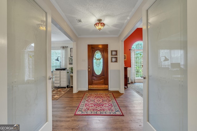 entryway with a textured ceiling, hardwood / wood-style flooring, a wealth of natural light, and crown molding