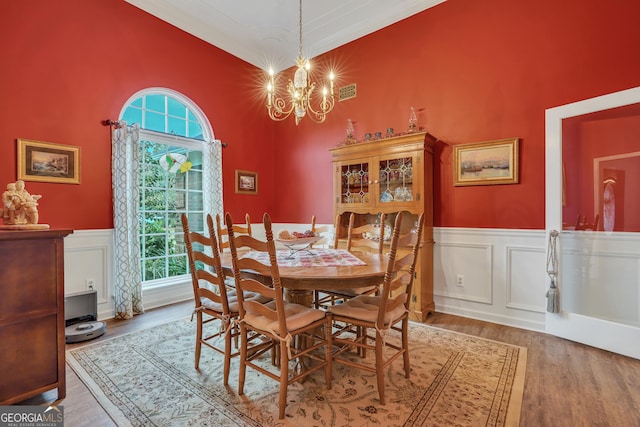 dining space with hardwood / wood-style floors, a towering ceiling, ornamental molding, and a chandelier