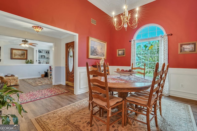 dining room featuring ceiling fan with notable chandelier, wood-type flooring, ornamental molding, and a high ceiling