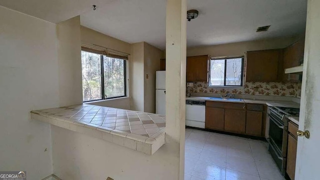 kitchen with tile counters, sink, backsplash, kitchen peninsula, and white appliances