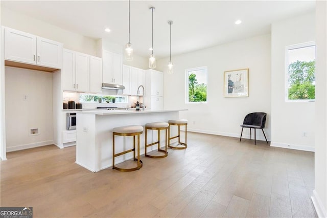 kitchen featuring hanging light fixtures, a kitchen breakfast bar, an island with sink, white cabinets, and light wood-type flooring