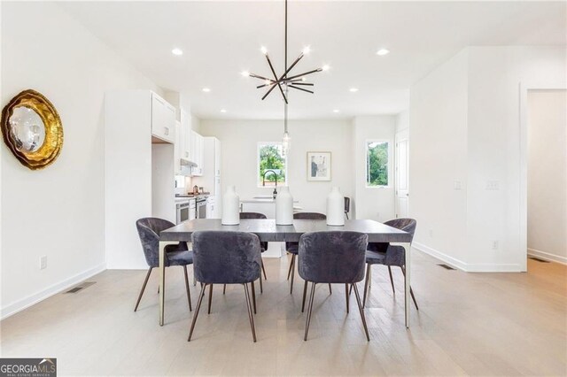 dining area featuring sink, light hardwood / wood-style flooring, and an inviting chandelier