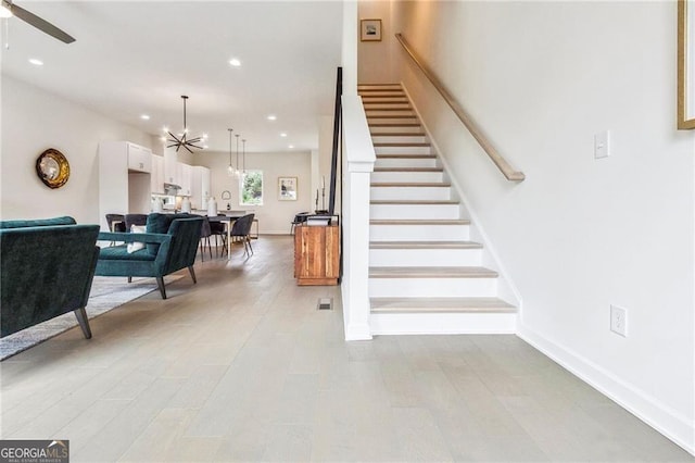 stairs featuring hardwood / wood-style floors and ceiling fan with notable chandelier