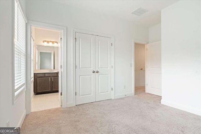 unfurnished bedroom featuring light colored carpet, ensuite bath, and a closet