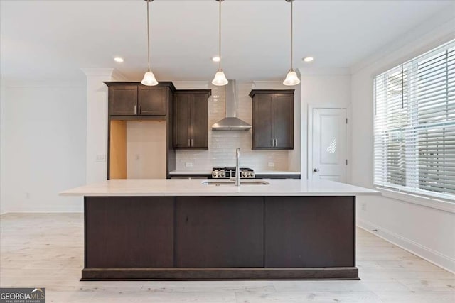 kitchen with dark brown cabinetry, a center island with sink, wall chimney exhaust hood, and pendant lighting