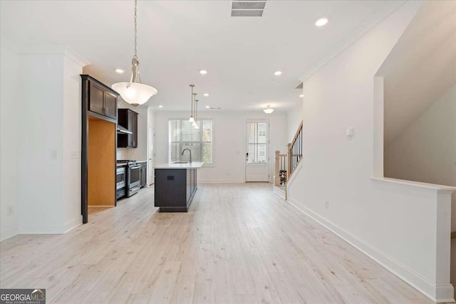 kitchen featuring sink, pendant lighting, light hardwood / wood-style floors, stainless steel range with gas cooktop, and an island with sink