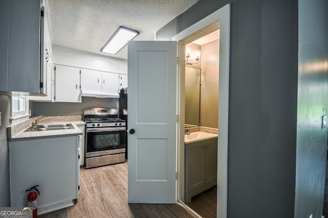 kitchen featuring white cabinetry, sink, stainless steel range with gas cooktop, light hardwood / wood-style flooring, and a textured ceiling