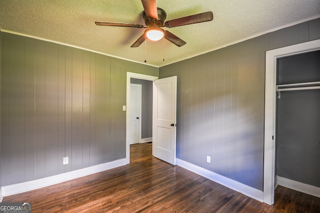 unfurnished bedroom with wooden walls, dark hardwood / wood-style floors, ceiling fan, a textured ceiling, and a closet