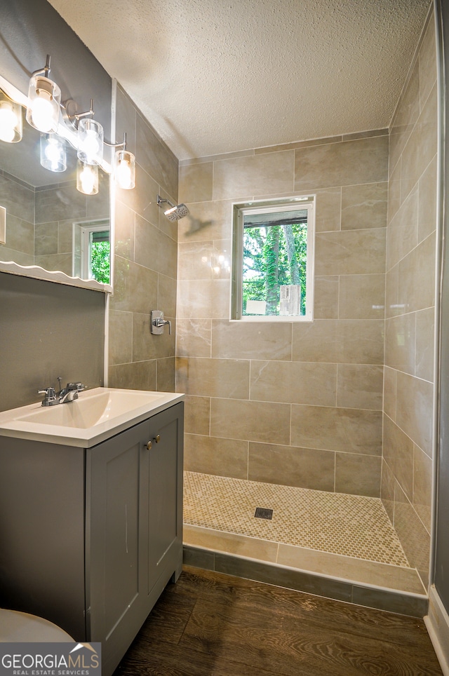 bathroom with hardwood / wood-style flooring, vanity, a textured ceiling, and tiled shower