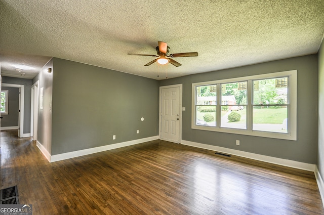 empty room with dark hardwood / wood-style floors, a healthy amount of sunlight, a textured ceiling, and ceiling fan