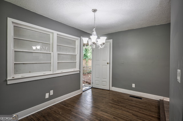 unfurnished dining area with dark hardwood / wood-style floors, a textured ceiling, and a chandelier