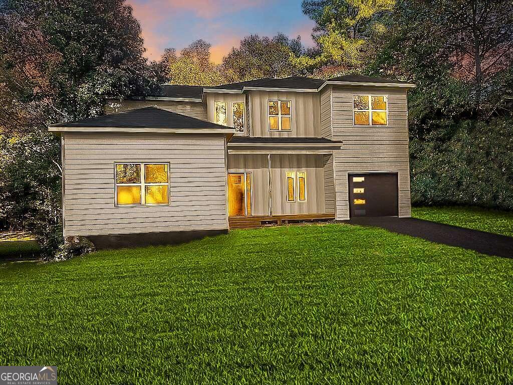 back house at dusk with a garage and a lawn