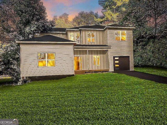 back house at dusk with a garage and a lawn