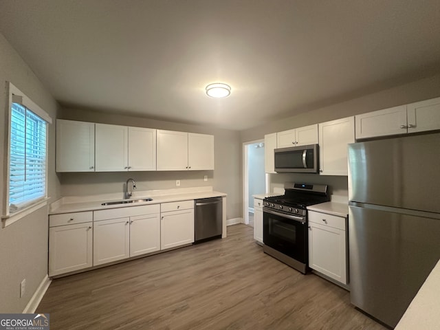 kitchen with wood-type flooring, appliances with stainless steel finishes, white cabinetry, and sink