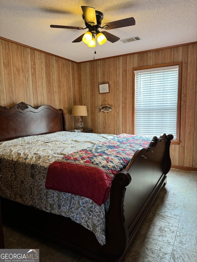 bedroom with a textured ceiling, ceiling fan, and wood walls