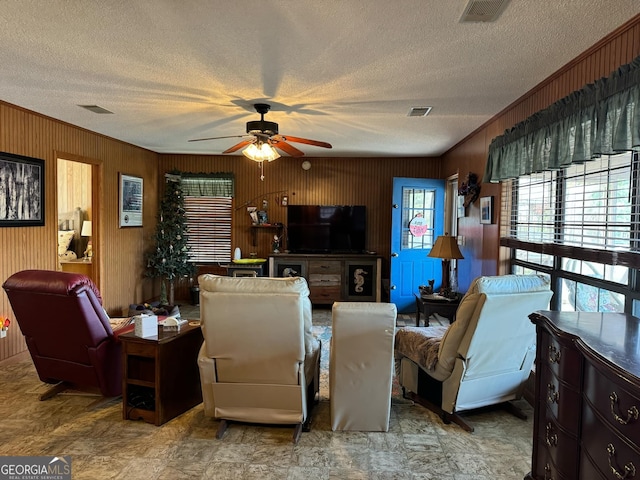 living room with a textured ceiling, ceiling fan, crown molding, and wood walls