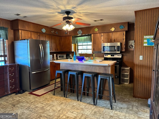 kitchen with appliances with stainless steel finishes, a breakfast bar, a textured ceiling, ceiling fan, and a center island