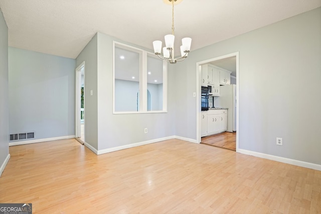 spare room with light wood-type flooring and a chandelier