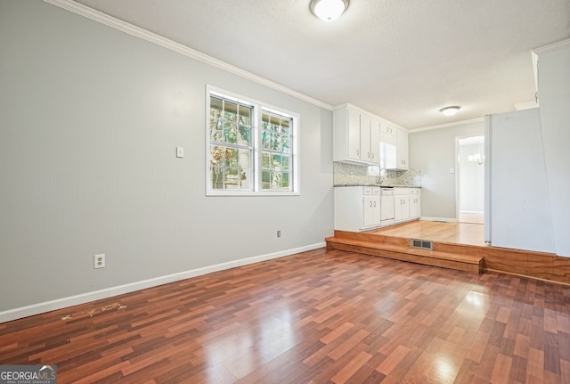 unfurnished living room with sink, dark wood-type flooring, a textured ceiling, and ornamental molding