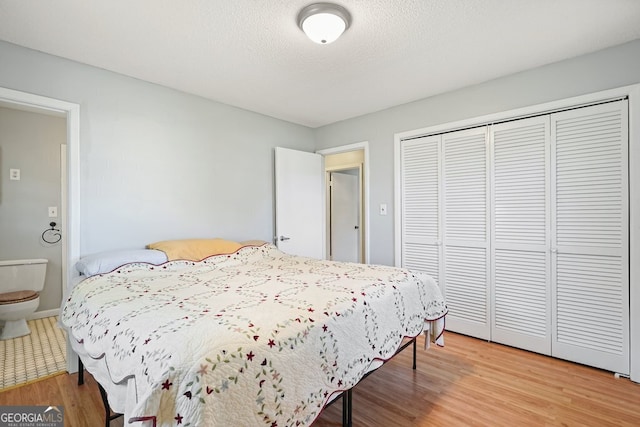 bedroom with ensuite bath, a closet, wood-type flooring, and a textured ceiling