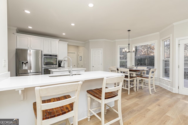 kitchen featuring light wood-type flooring, stainless steel appliances, sink, pendant lighting, and white cabinets