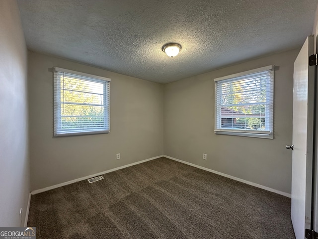 spare room featuring dark colored carpet and a textured ceiling