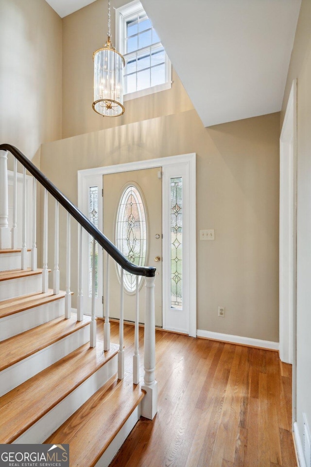 entryway featuring a chandelier, wood-type flooring, a towering ceiling, and a healthy amount of sunlight