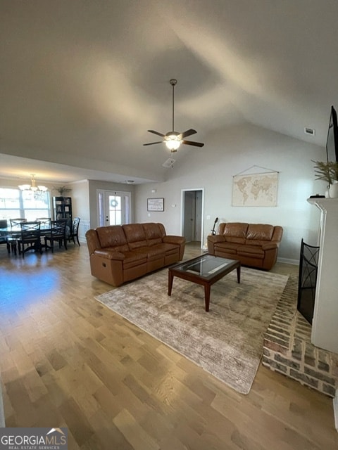 living room with hardwood / wood-style floors, ceiling fan with notable chandelier, and vaulted ceiling