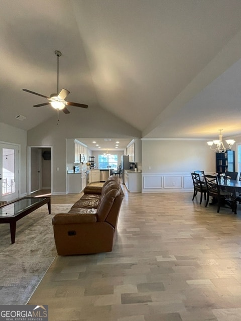 living room featuring lofted ceiling, ceiling fan with notable chandelier, light hardwood / wood-style floors, and a healthy amount of sunlight