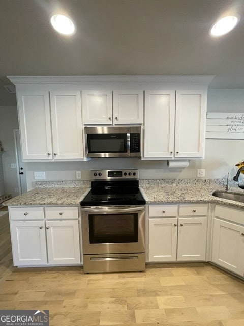 kitchen featuring white cabinets, sink, light stone countertops, light wood-type flooring, and appliances with stainless steel finishes