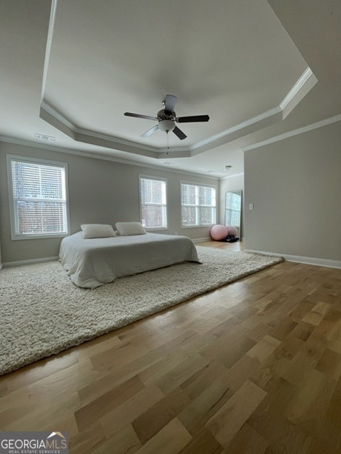 unfurnished bedroom with a raised ceiling, wood-type flooring, and multiple windows